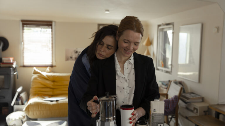 Standbild aus dem Film "Wunderschöner": Vicky (Nora Tschirner) umarmt Sonja (Karoline Herfurth) von hinten innig in der Küche beim Kaffee eingiessen.